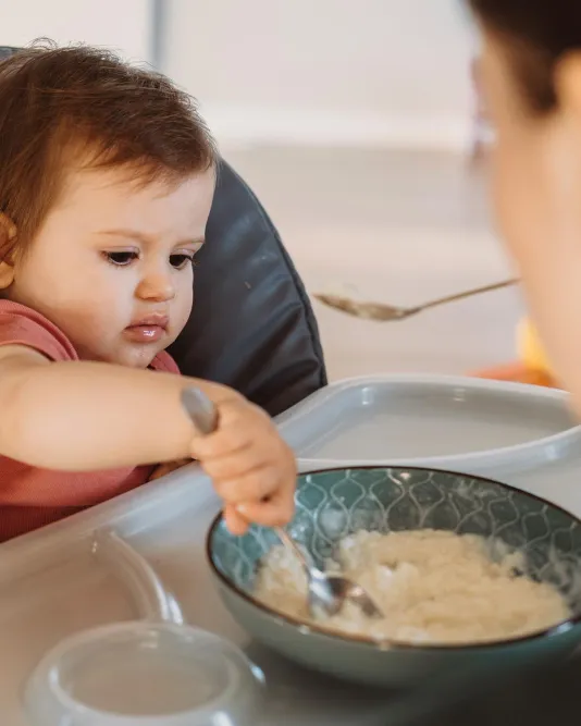Bébé participant à son repas accompagné d'un adulte